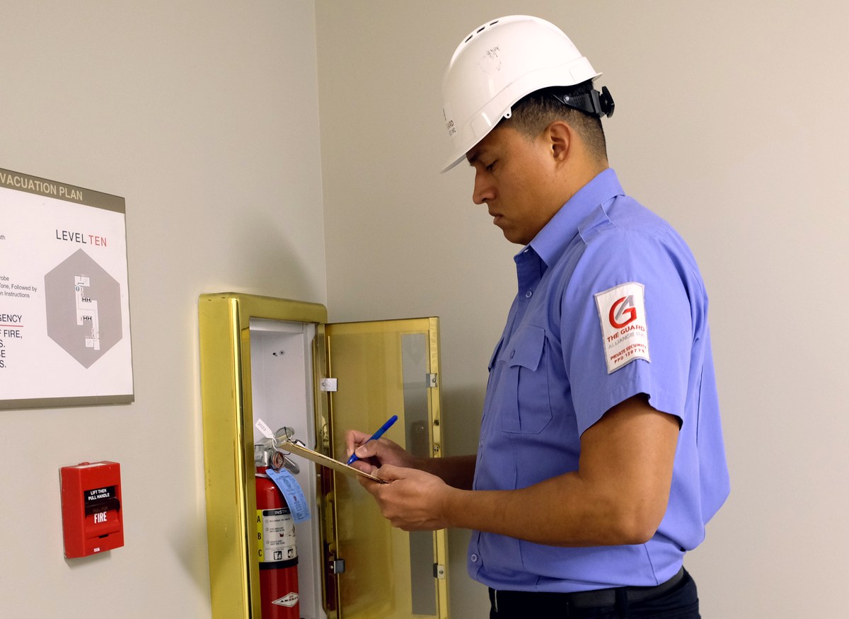 TGA fire watch guard in a hard hat logging a fire extinguisher and alarm pull station inspection
